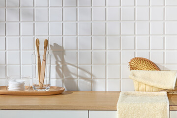 Japandi bathroom scene with soft towels and bamboo brushes placed on a wooden tray. Sunlight glides...
