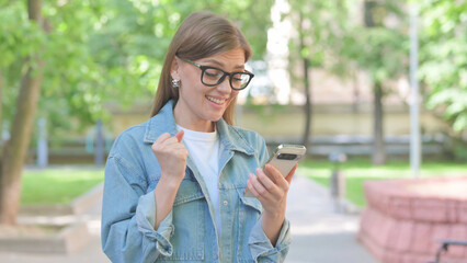Young Woman Celebrating with Phone Outdoors