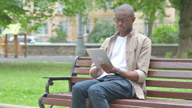 Young African Man Using a Digital Tablet on a Park Bench