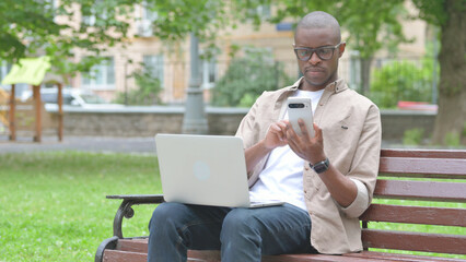 Young African Man Using Smartphone and Laptop Outdoors