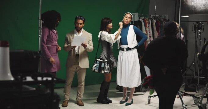 Woman, actress and makeup artist on film set for face, director and cameraman for production. People, cosmetics and touchup with green screen, cinematography or recording equipment at movie studio