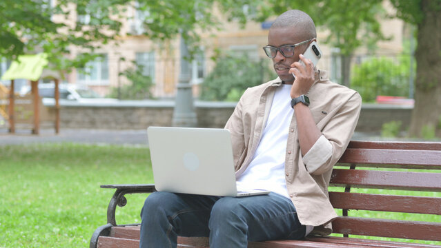 Young African Man Talking on Phone While Using Laptop