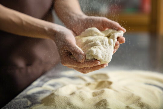 Person kneading dough in kitchen shaping pizza base carefully preparing meal