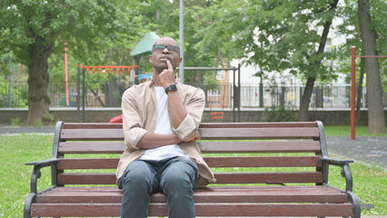 Fototapeta premium Pensive African Man Sitting Outdoor on Bench