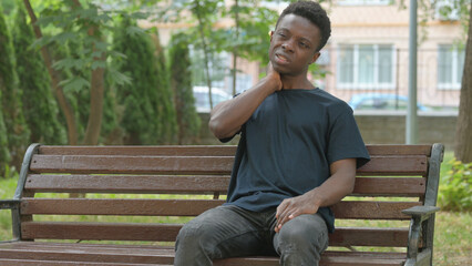 Obraz premium Casual African Man Massaging Her Neck on a Park Bench