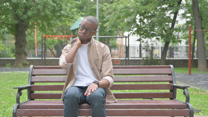 Obraz premium African Man with Neck Pain Sitting Outdoor on Bench