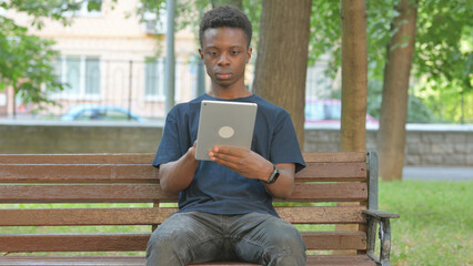 Casual African Man Using a Digital Tablet on a Park Bench