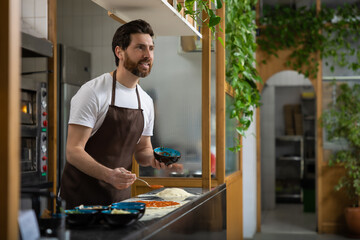 Man prepares pizza in kitchen spreading sauce carefully creating meal