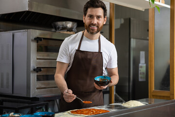 Man finishes pizza in kitchen arranging toppings carefully completing meal