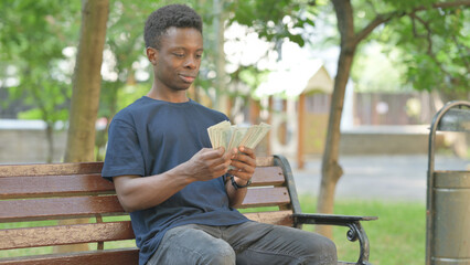 African American Man Counting Money while Sitting Outdoor