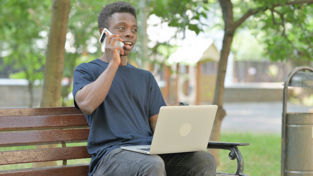 African American Man Talking on Phone While Using Laptop while Sitting Outdoor