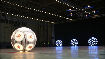 Large illuminated spheres in a spacious indoor venue with drone overhead.