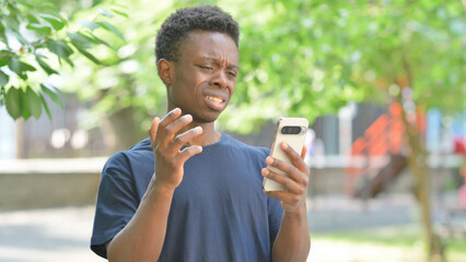 Upset Casual African Man Reacting to Phone Content Outdoors
