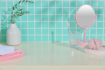 A soft blue-green bathroom setup with flower vase, pink mirror and skincare tools on beige counter....
