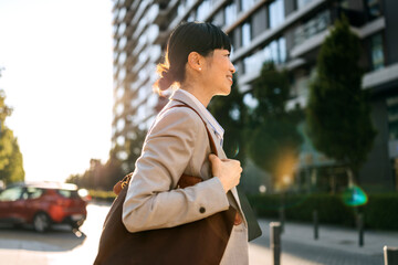 Focused woman walking confidently in an urban area during golden hour carrying a tote bag