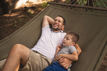 Father and son 5 years old fooling around playing relaxing in a hammock outdoors in a pine forest...