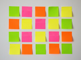Organized grid of twenty colorful sticky notes close up, pink, yellow, orange and green, arranged neatly on a light white wall. Minimal and clean layout, arranged neatly on a light white wall.