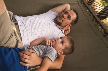 Father and son 5 years old fooling around playing relaxing in a hammock outdoors in a pine forest...