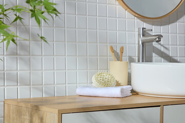 White sink beside bamboo toothbrushes, sponge, and towel on a wood surface. The soft greenery and...