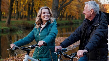 Elderly couple riding bicycles along a picturesque riverbank path, surrounded by vibrant autumn foliage, sharing laughter and enjoying each other's company during a leisurely afternoon ride