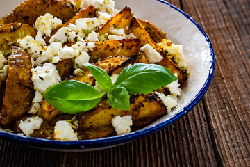 Greek style roasted potatoes with feta cheese on wooden table