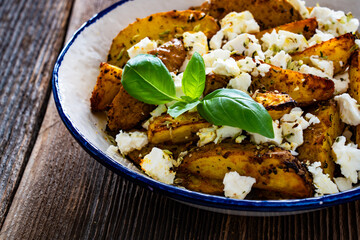 Greek style roasted potatoes with feta cheese on wooden table