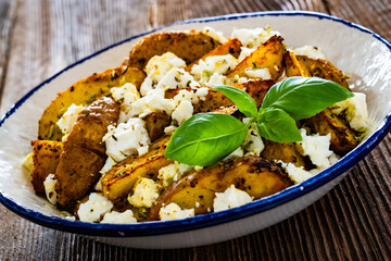 Greek style roasted potatoes with feta cheese on wooden table