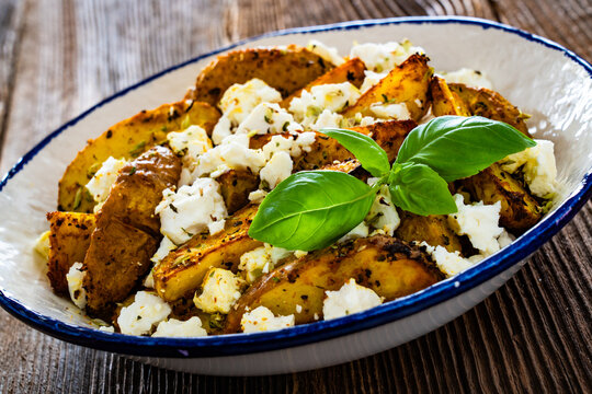 Greek style roasted potatoes with feta cheese on wooden table