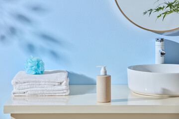 Rolled towels and pump bottle rest beside a ceramic sink under a light blue wall. Clean...