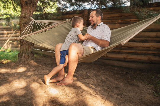 Father and son 5 years old fooling around playing relaxing in a hammock outdoors in a pine forest at a campsite. Tourism, active recreation, time spent with children