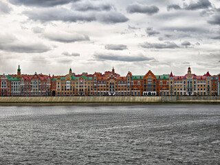 Fototapeta premium Colorful historic buildings line the Bruges embankment by the river in Yoshkar-Ola under a cloudy sky