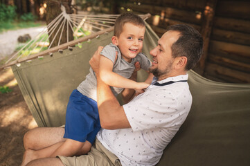 Father and son 5 years old fooling around playing relaxing in a hammock outdoors in a pine forest at a campsite. Tourism, active recreation, time spent with children