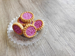 Round baked sweet biscuits with bright red filling and pink pastry sprinkles, on a decorative plate