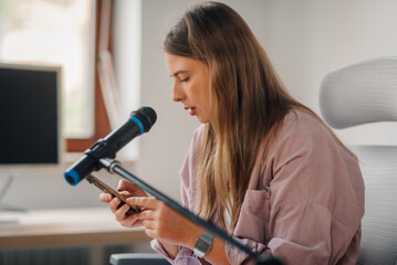 Young woman recording podcast using smartphone and microphone