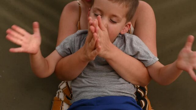 mother son 5 years old fooling around playing relaxing in a hammock outdoors in a pine forest at a campsite. Tourism, active recreation, time spent with children closeup  claps his hands