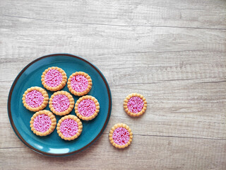 Round baked sweet biscuits with bright red filling and pink pastry sprinkles, on a decorative plate