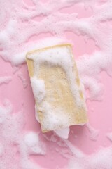 Soap bar with foam on pink background, top view