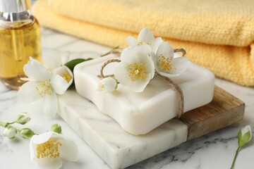Soap bar, cosmetic product and jasmine flowers on white marble table, closeup