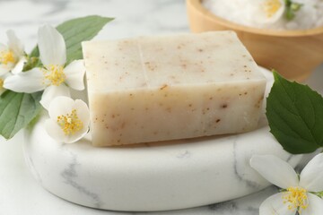 Soap bar, sea salt and jasmine flowers on white marble table, closeup