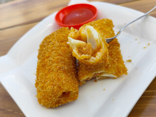 Crispy golden rissoles with savory and delicious filling, served on an elegant white plate, accompanied by a small bowl filled with bright red chili sauce and a fork, on the menu at an outdoor cafe.