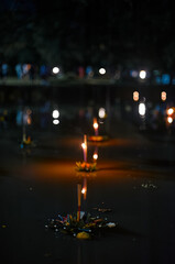 Krathongs decorated with flowers and candles drift on a serene water surface, creating a peaceful...