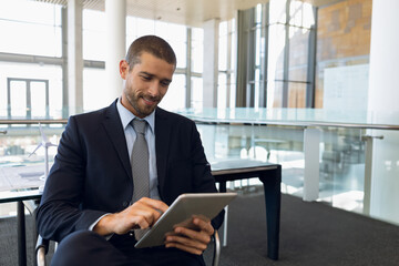 Fototapeta premium Male professional sitting at office lobby table using tablet beside wind turbine model and papers
