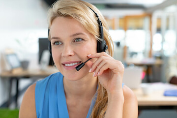 Female customer support agent answering calls in open office using headset and computer monitors