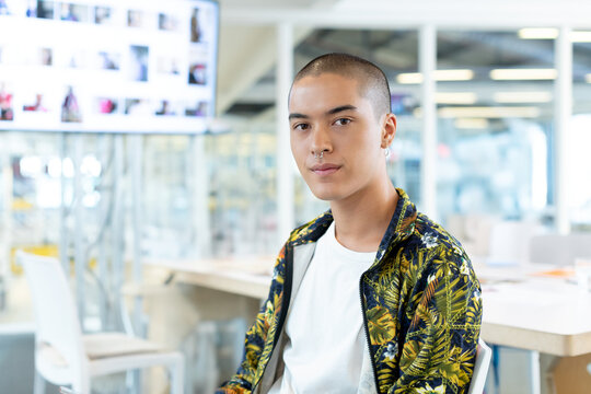Asian man sitting at work table in creative studio reviewing thumbnail visuals on display