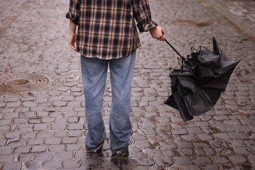 Woman with broken umbrella on wet pavement outdoors, closeup