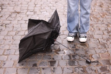 Woman and broken umbrella on wet pavement outdoors, closeup
