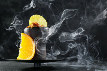 Hookah bowl with citrus fruits and smoke on black table, closeup