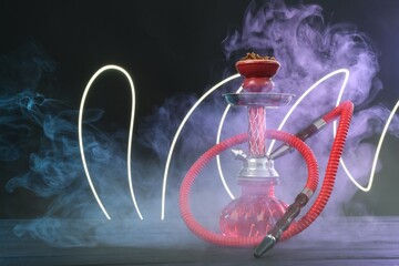 Hookah on wooden table with smoke in color lights against black background