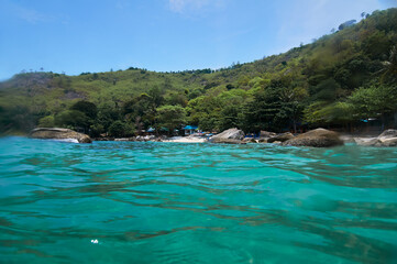 Vibrant tropical beach photographed from the turquoise waters with lush green hillsides and a clear...