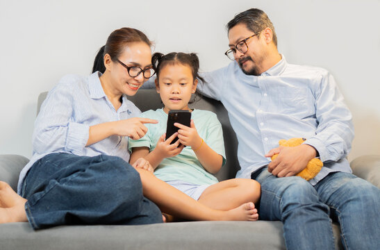 Cheerful young family with kids laughing watching funny video on smartphone sitting on couch together. - Powered by Adobe